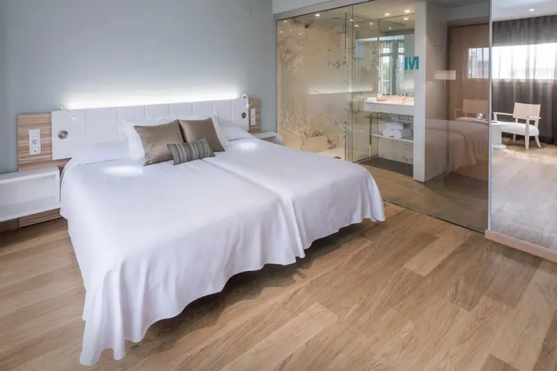 Une chambre lumineuse avec un grand lit et une salle de bain vitrée.