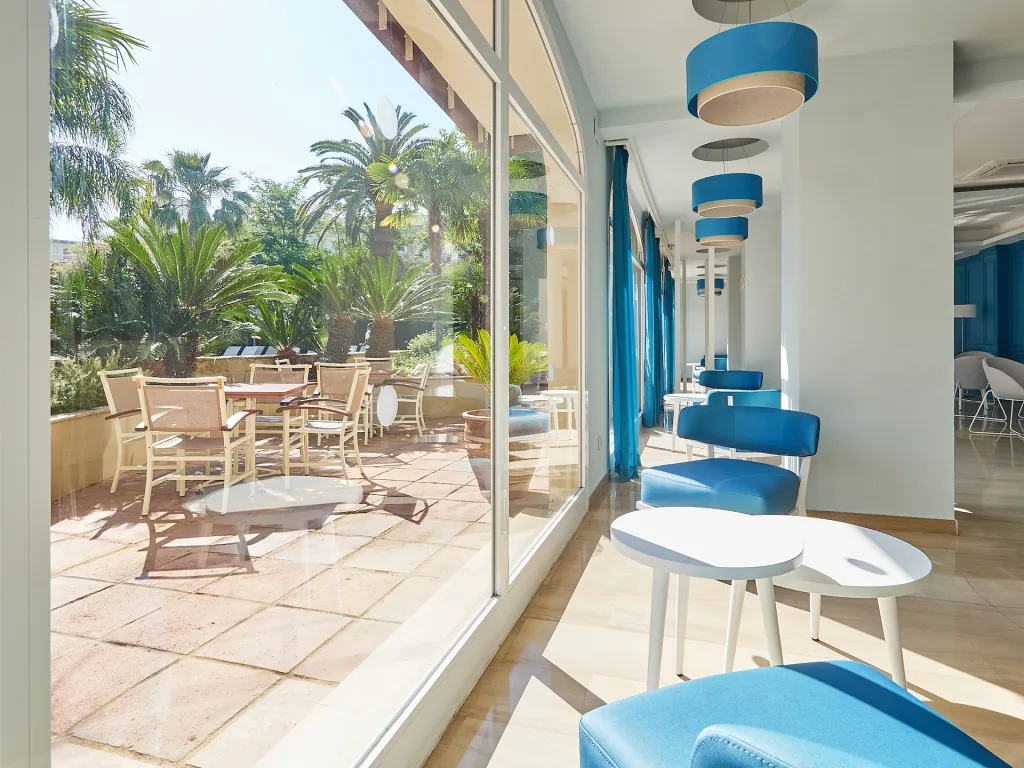 Espace de détente intérieur avec mobilier bleu et vue sur une terrasse ombragée.