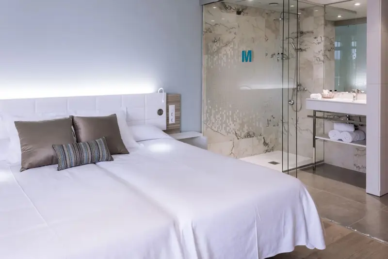 Une chambre lumineuse avec un grand lit et une douche à l'italienne en verre.