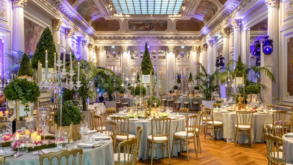 Une salle de réception lumineuse est mise en scène avec des tables dressées et une végétation luxuriante.