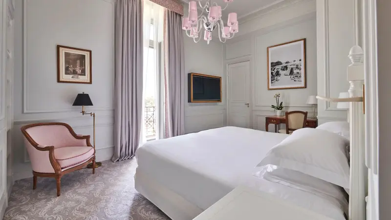 Chambre lumineuse avec un lit blanc et un fauteuil rose.