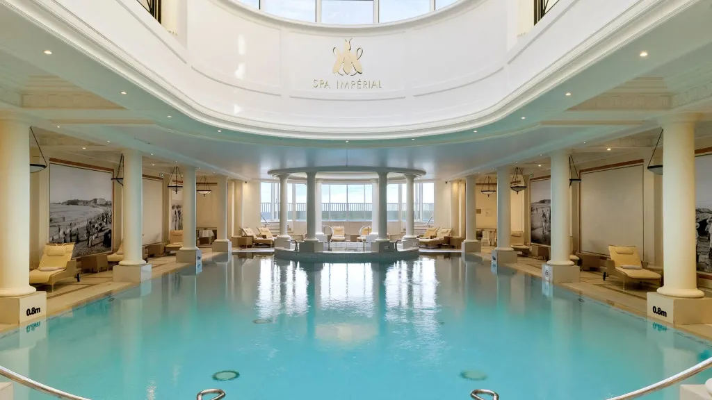 Une piscine intérieure lumineuse avec des transats alignés le long des fenêtres.
