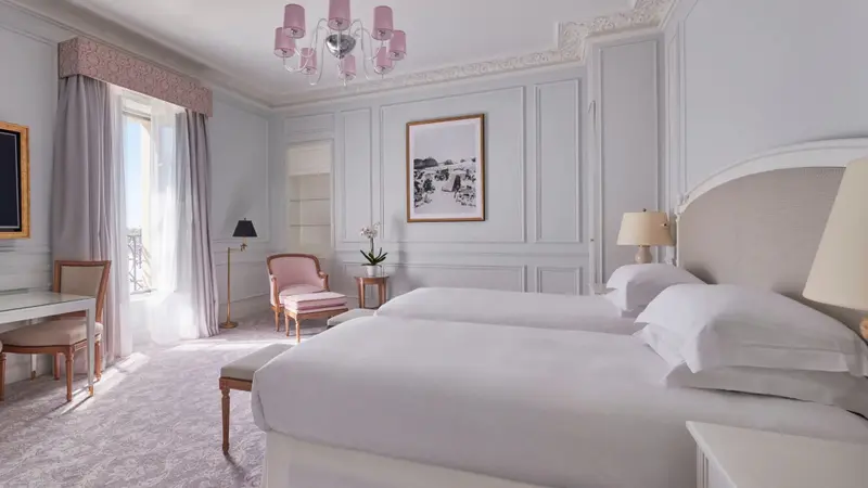 Une chambre lumineuse avec deux lits simples et un bureau près de la fenêtre.