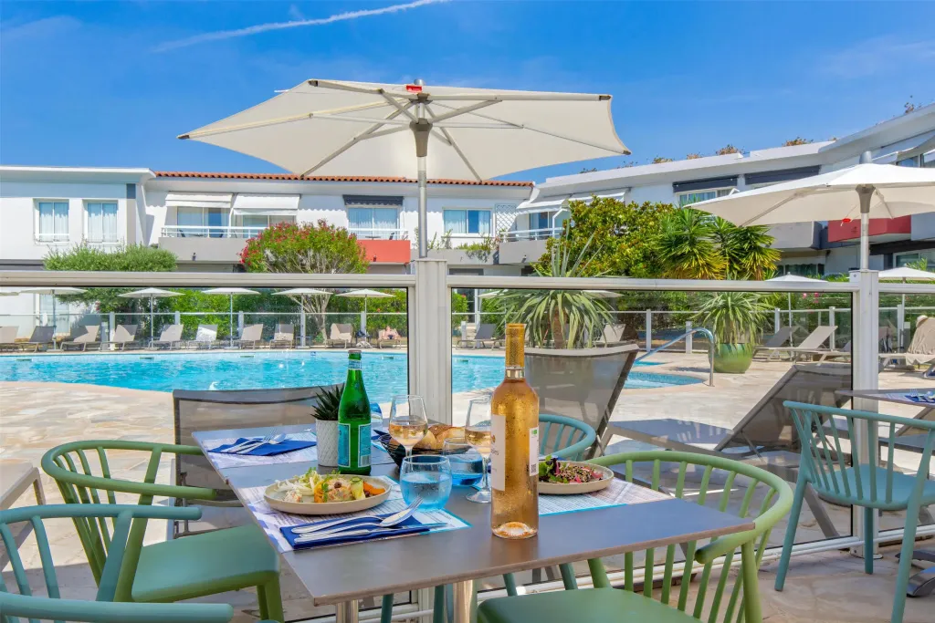Une table est dressée avec des plats et des boissons près d'une piscine ensoleillée.