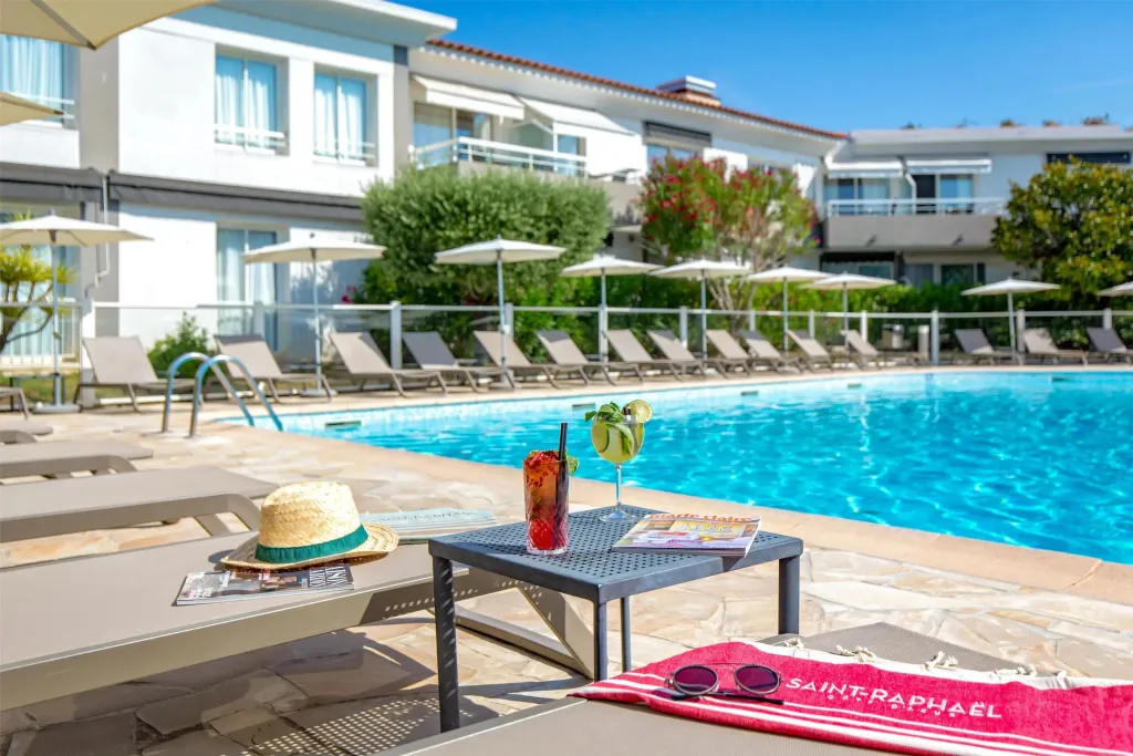 Transats et table basse avec boisson au bord d'une piscine ensoleillée.