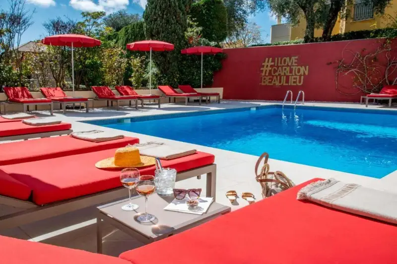 Transats rouges bordent une piscine bleue ensoleillée.