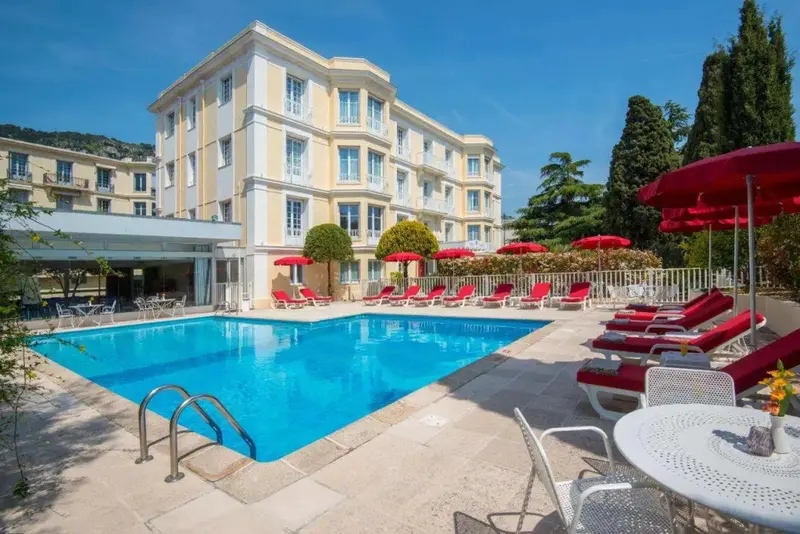 Une piscine ensoleillée avec des transats rouges devant un bâtiment jaune.