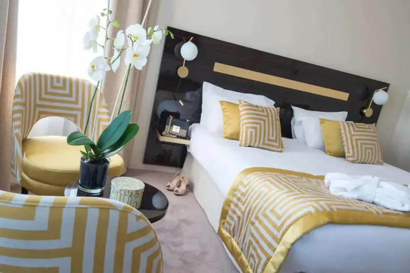 Une chambre lumineuse avec un lit fait et des fauteuils décoratifs.