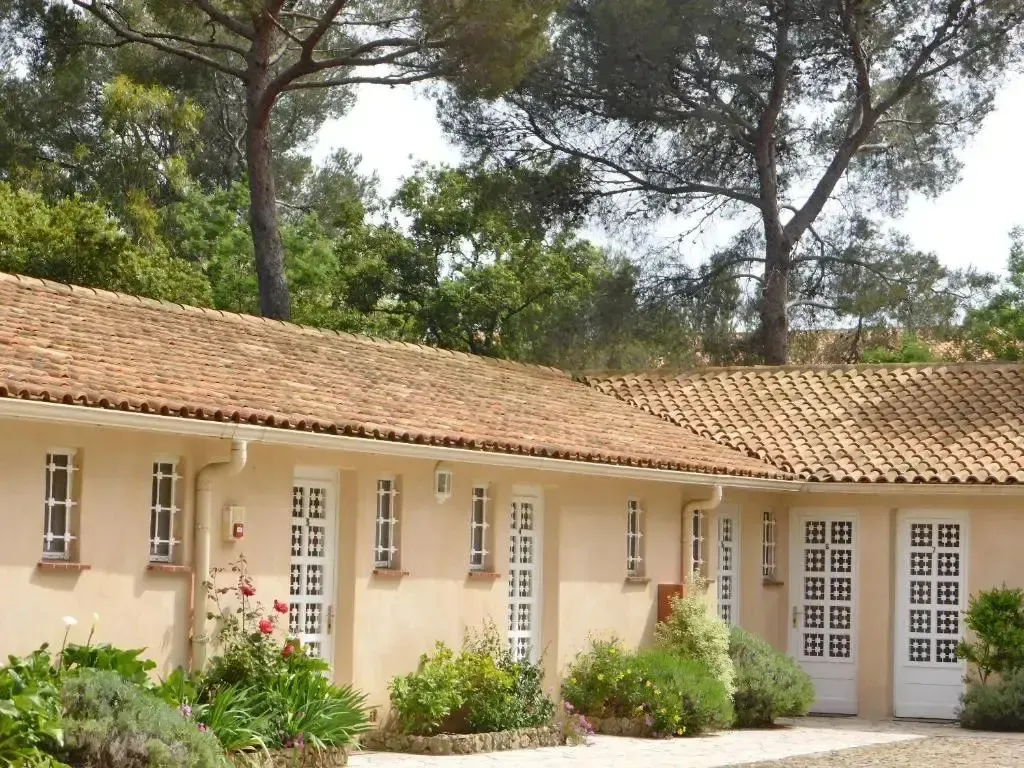 Façade d'un bâtiment beige avec des fenêtres et des volets verts, entouré de végétation.