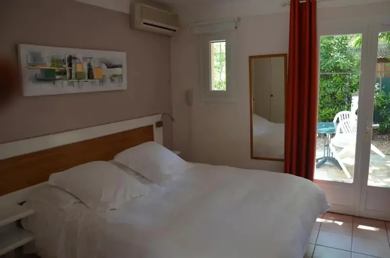 Une chambre lumineuse avec un grand lit et une porte-fenêtre donnant sur une terrasse.