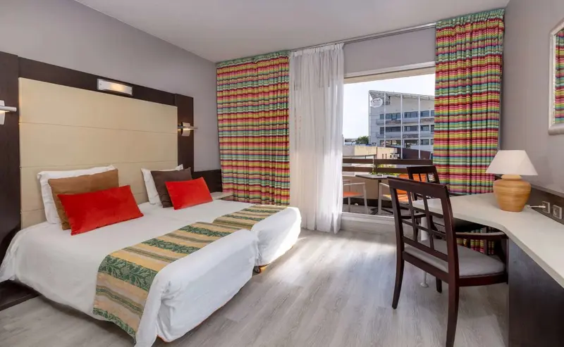 Une chambre lumineuse avec un lit double et un bureau près d'une baie vitrée.
