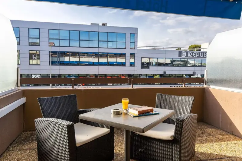 Une table et des chaises en osier sont disposées sur une terrasse avec vue sur un bâtiment.