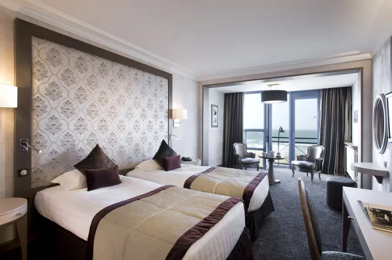 Une chambre lumineuse avec deux lits simples et un coin salon donnant sur la mer.