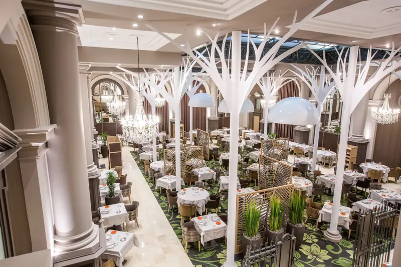 Une salle de restaurant spacieuse avec des tables dressées et une décoration arborée.