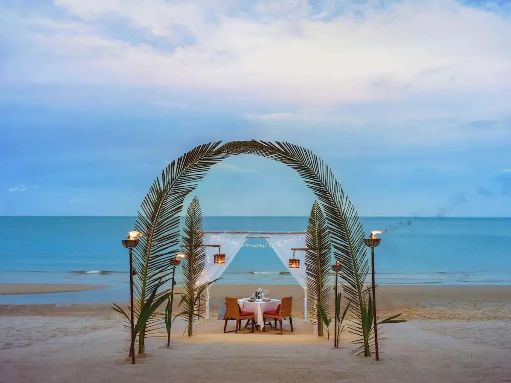 Table dressée sur une plage de sable fin au coucher du soleil.