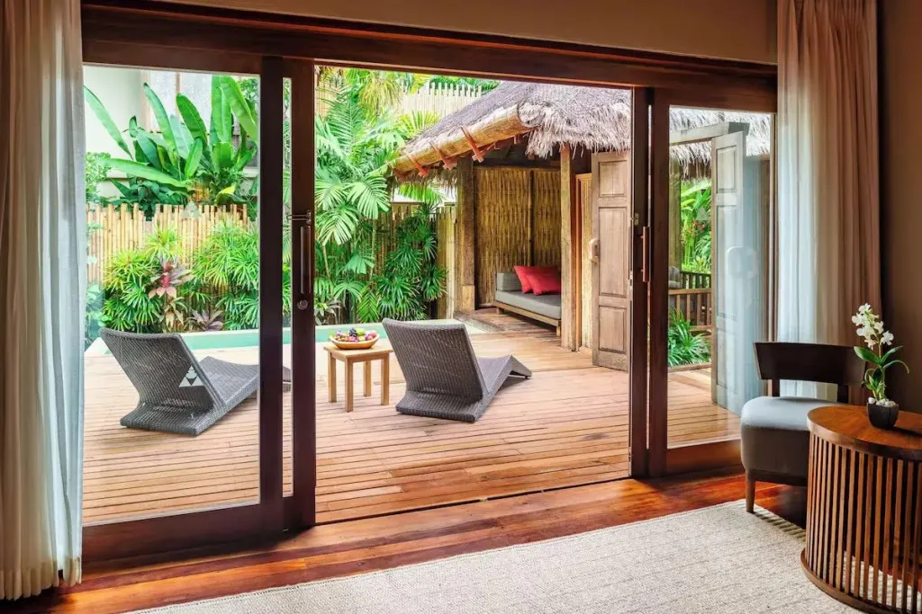 Une terrasse en bois avec deux chaises longues donne sur une petite piscine et un espace de détente extérieur.