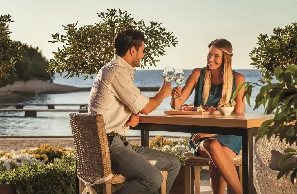 Un couple trinque avec des verres de vin à une table en extérieur.
