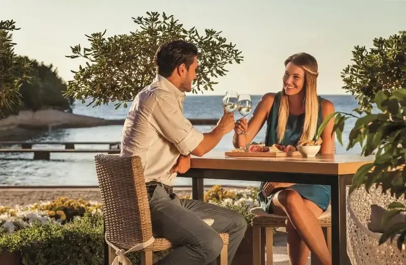 Un couple trinque avec des verres de vin à une table en extérieur.