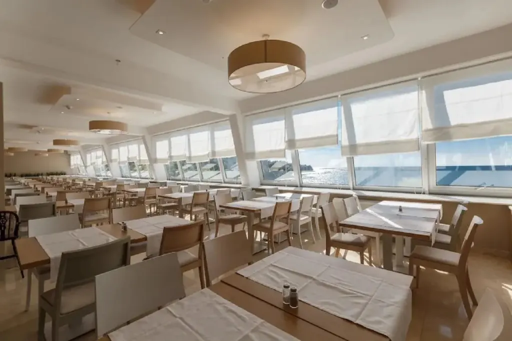 Une salle lumineuse avec des tables dressées face à une vue sur la mer.