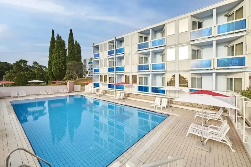 Piscine ensoleillée devant un bâtiment aux balcons colorés.