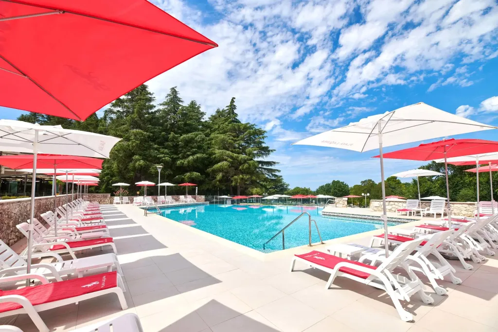 Transats rouges et blancs disposés autour d'une piscine ensoleillée.