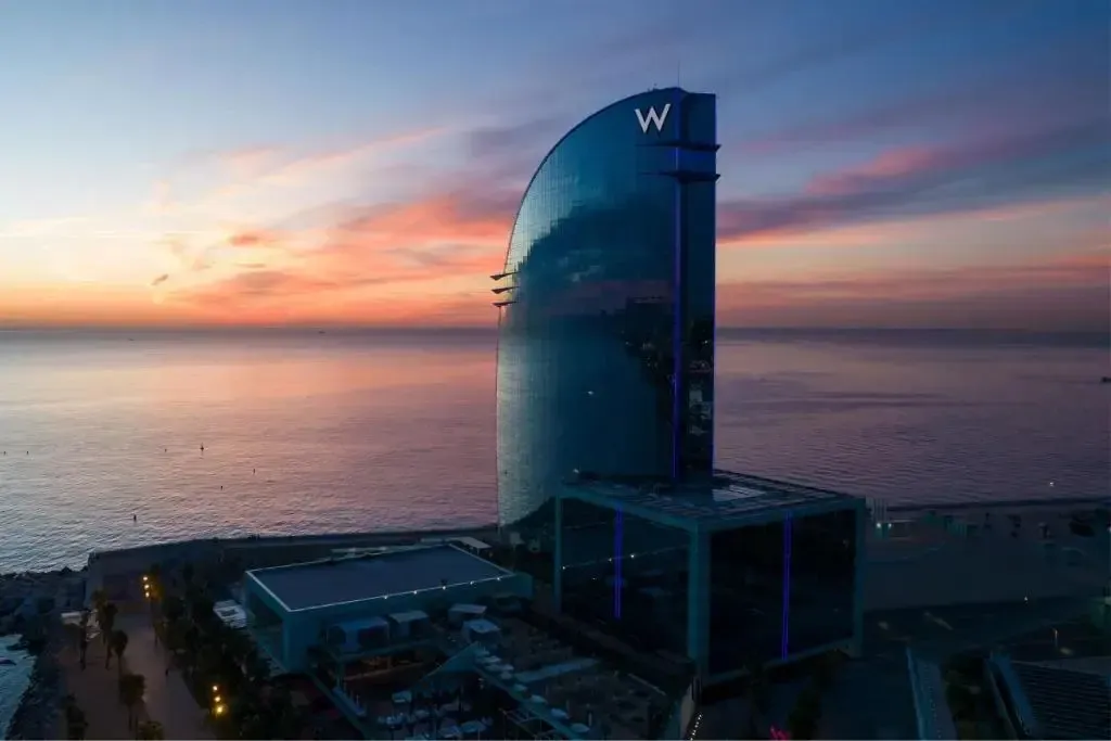Bâtiment moderne en verre surplombant la mer au coucher du soleil.
