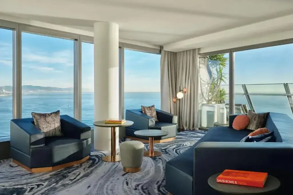 Un espace de détente intérieur avec des fauteuils et un canapé face à une grande baie vitrée donnant sur la mer.