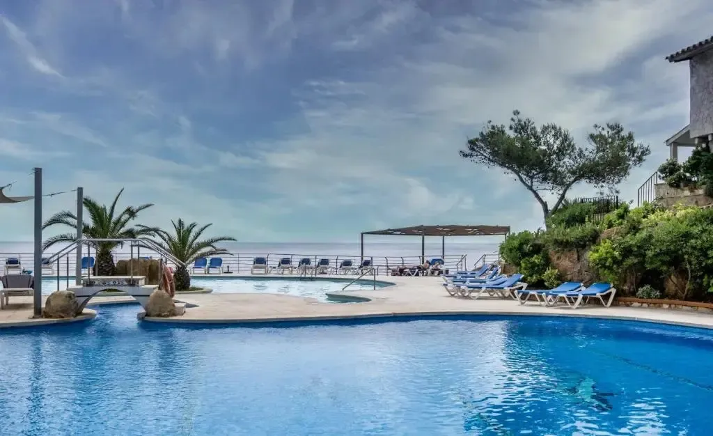 Une piscine bleue bordée d'une terrasse avec des transats et des palmiers.