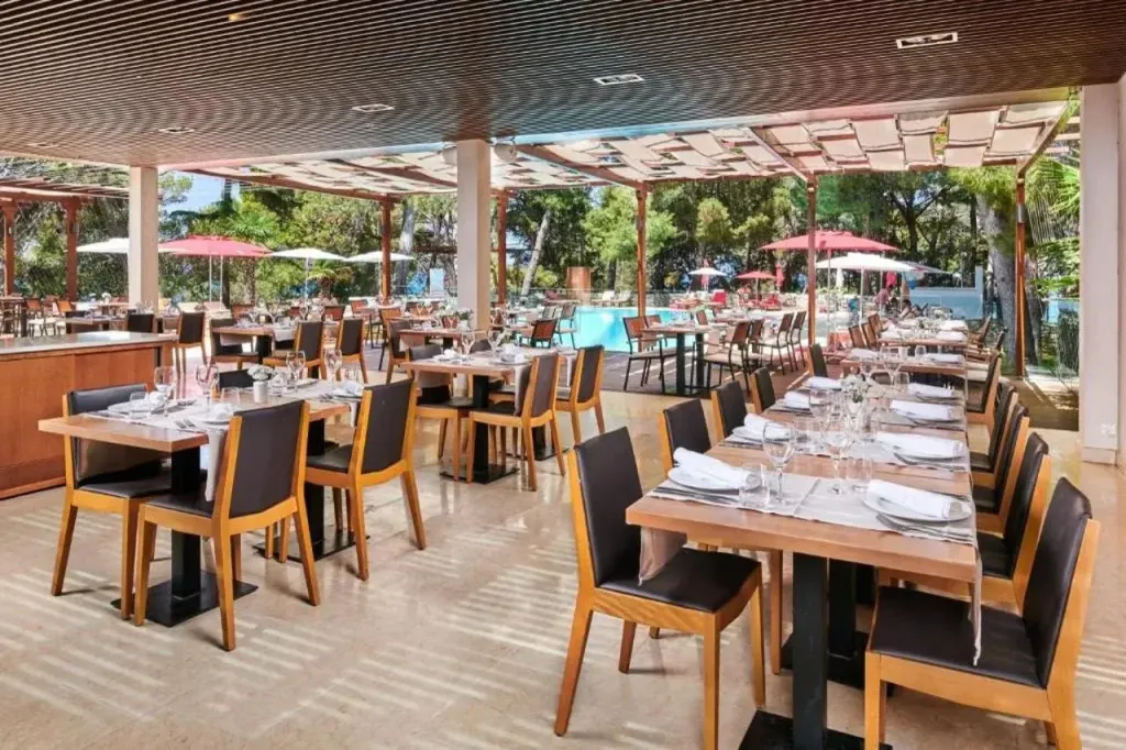 Une salle de restaurant lumineuse avec des tables dressées et une vue sur une piscine.