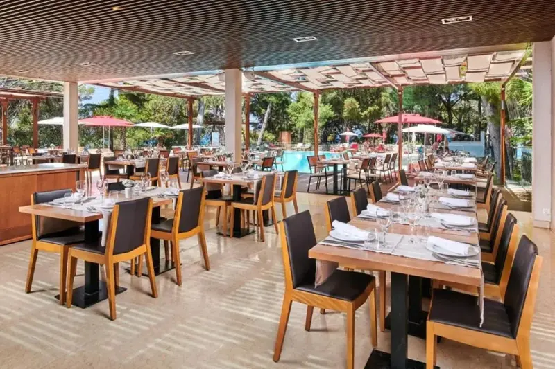 Une salle de restaurant lumineuse avec des tables dressées et une vue sur une piscine.