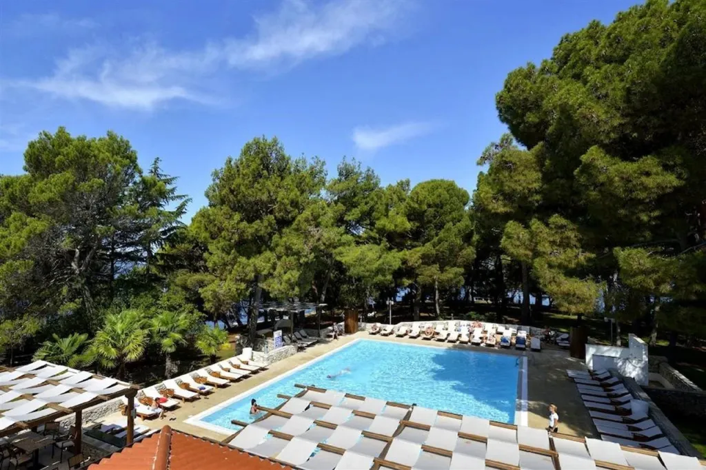 Une piscine rectangulaire bordée de transats sous des parasols, entourée de végétation luxuriante et avec une vue sur la mer.