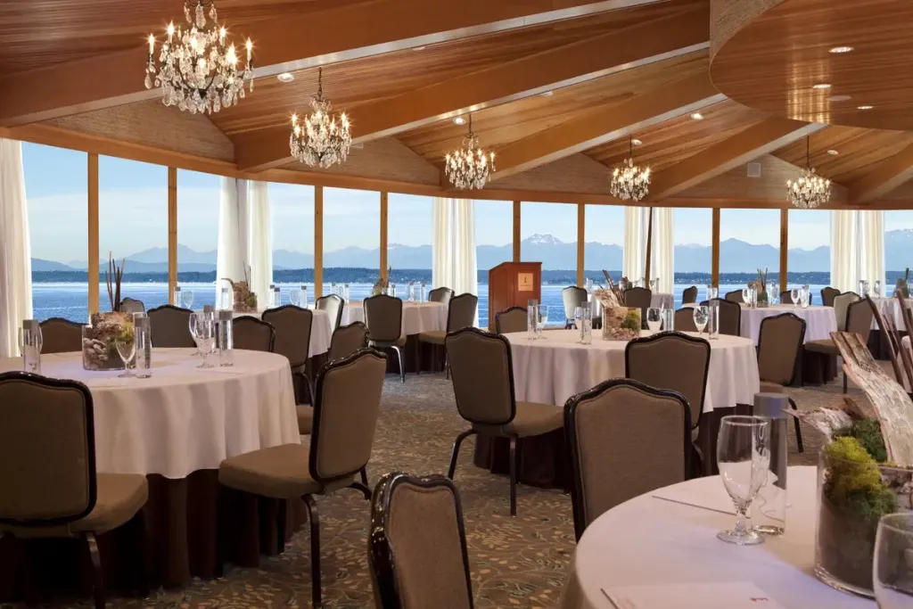 Une salle lumineuse avec de grandes fenêtres donnant sur la mer et des tables dressées pour un repas.