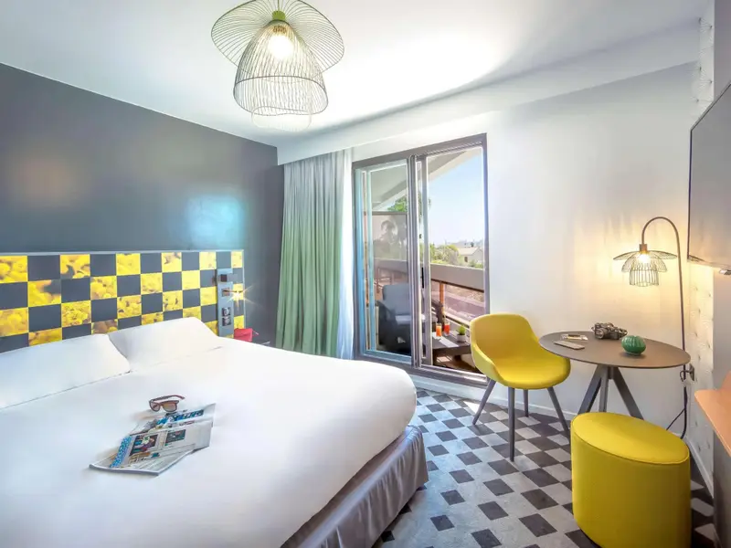 Une chambre lumineuse avec un lit blanc et un coin salon coloré.