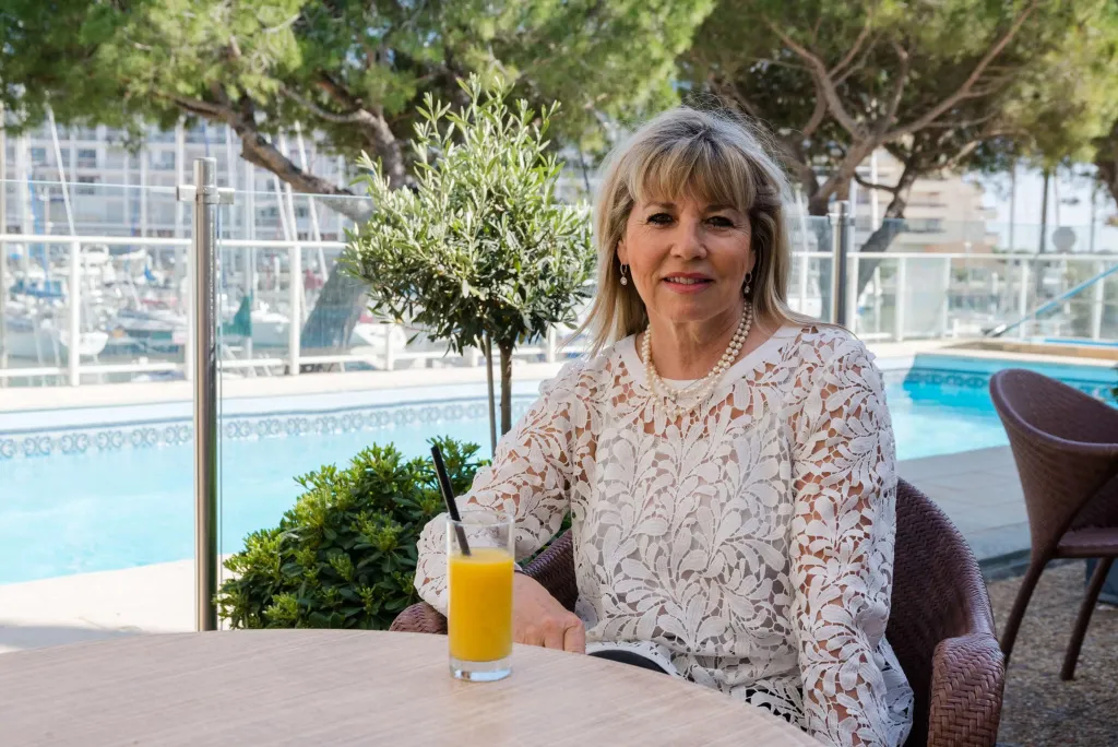 Une femme assise à une table avec une boisson fraîche, près d'une piscine.