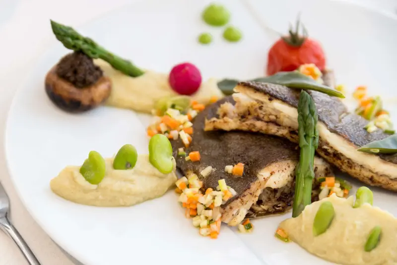 Assiette raffinée avec un plat de poisson, des légumes et une sauce colorée.