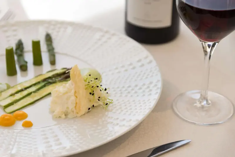 Assiette raffinée avec des légumes et une préparation crémeuse, accompagnée d'un verre de vin rouge.