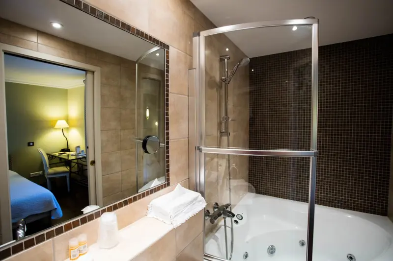 Une salle de bain avec baignoire et douche à l'italienne donne sur une chambre lumineuse.