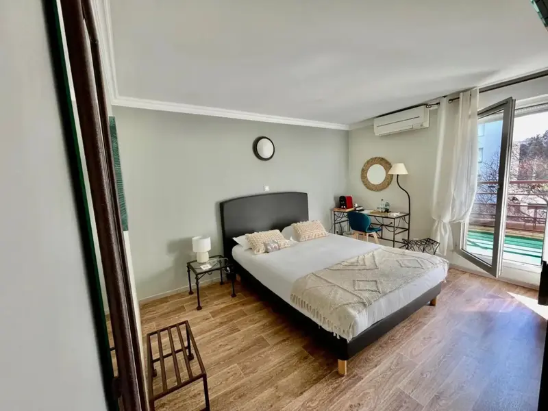 Une chambre lumineuse avec un grand lit et un bureau près d'une baie vitrée.