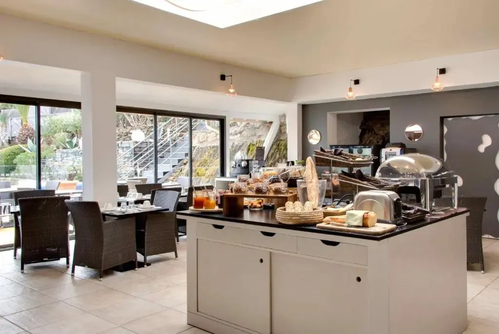 Une salle lumineuse avec des tables et des chaises, un buffet de petit-déjeuner et de grandes baies vitrées.
