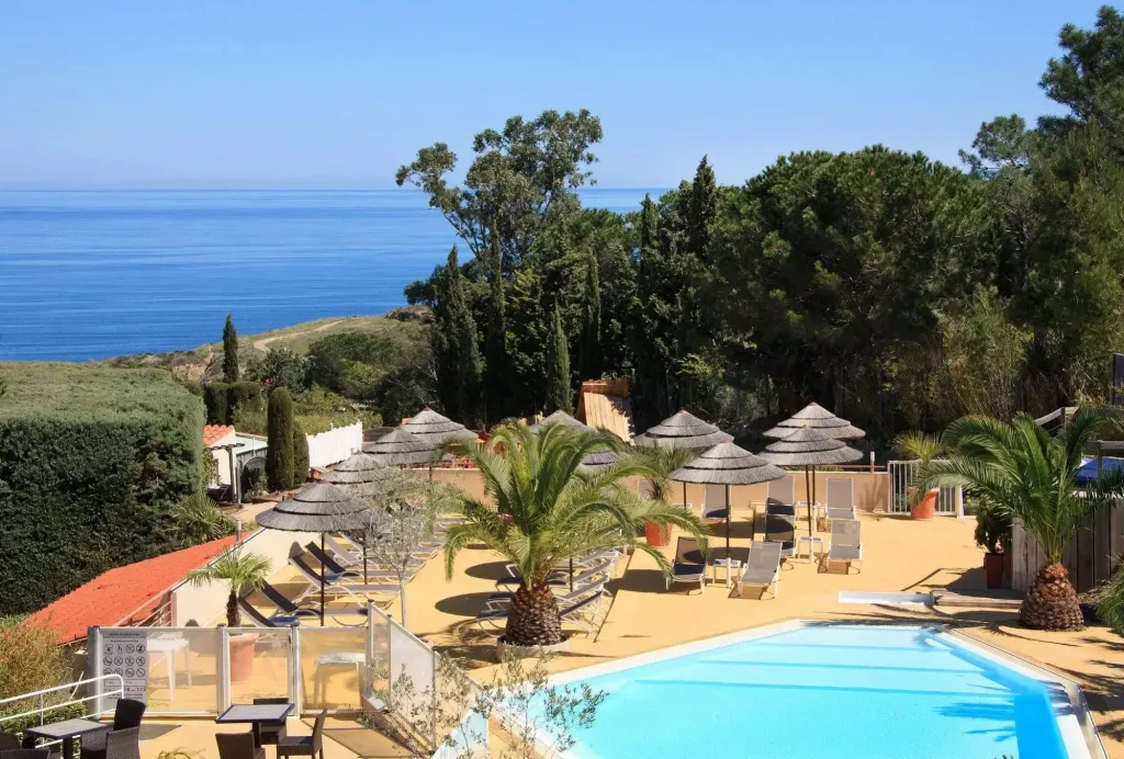Une piscine avec des transats et des parasols offre une vue sur la mer.