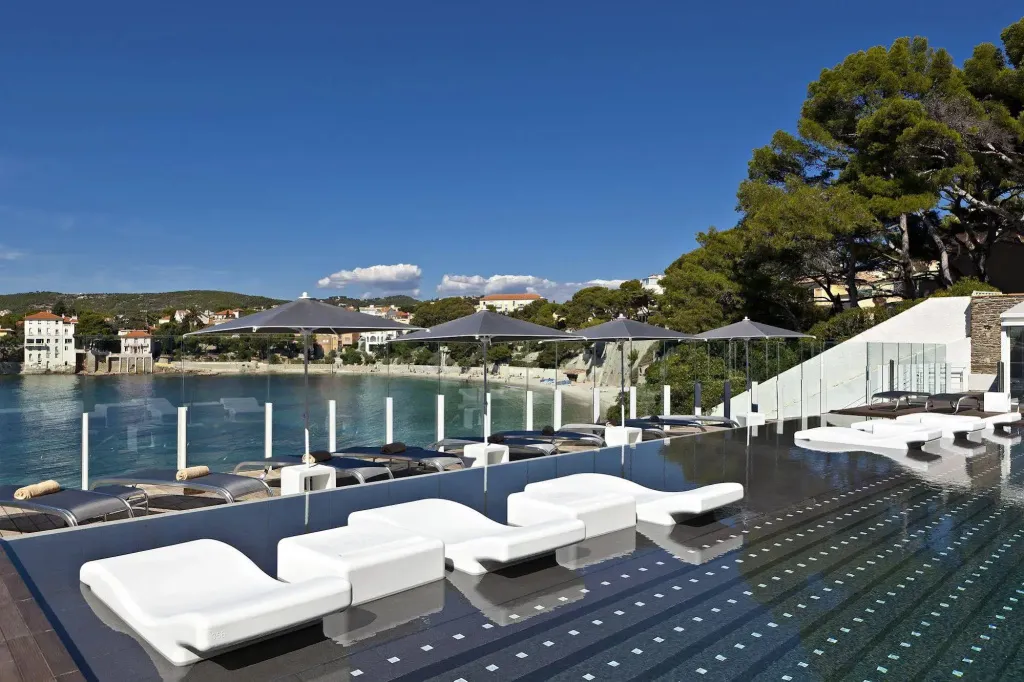 Transats blancs alignés au bord d'une piscine à débordement avec vue sur la mer.