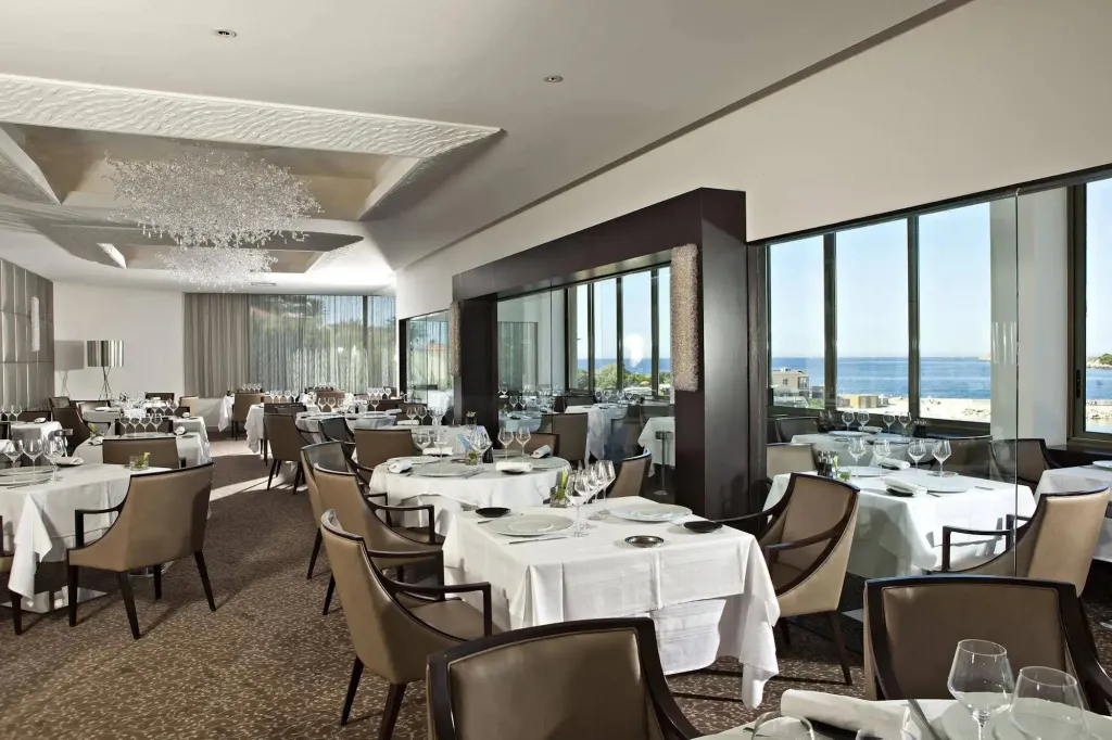 Une salle lumineuse avec des tables dressées face à une vue sur la mer.