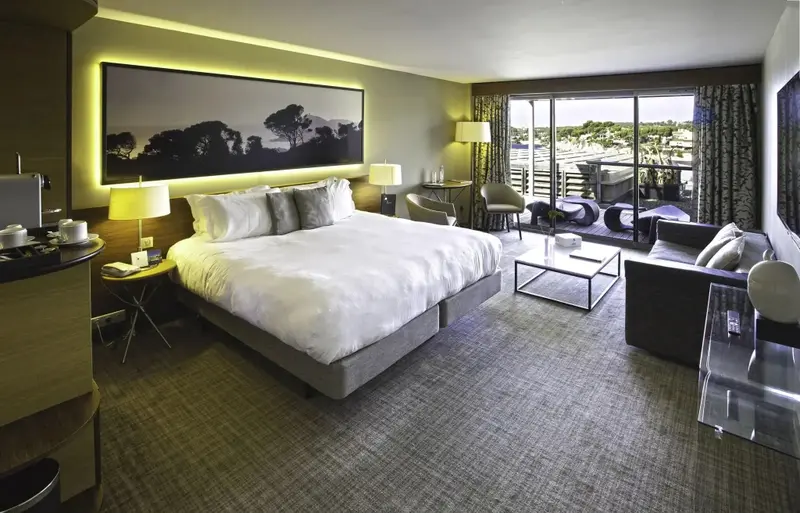 Une chambre lumineuse avec un grand lit et un coin salon donnant sur une terrasse.