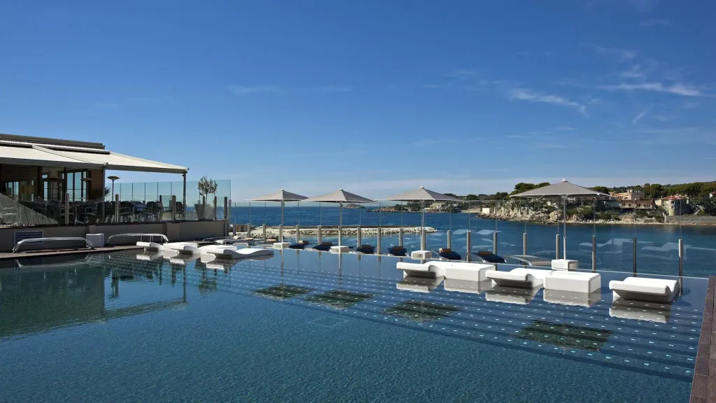 Transats blancs alignés au bord d'une piscine à débordement avec vue sur la mer.