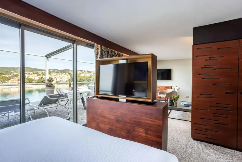 Une chambre lumineuse avec un grand lit et une vue sur la mer depuis une terrasse.