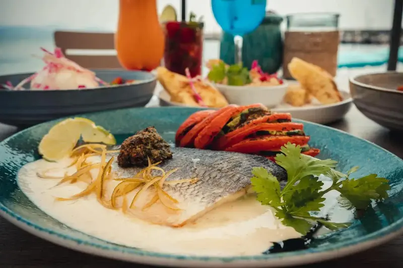 Assiette de poisson grillé agrémentée de légumes et de sauce blanche.