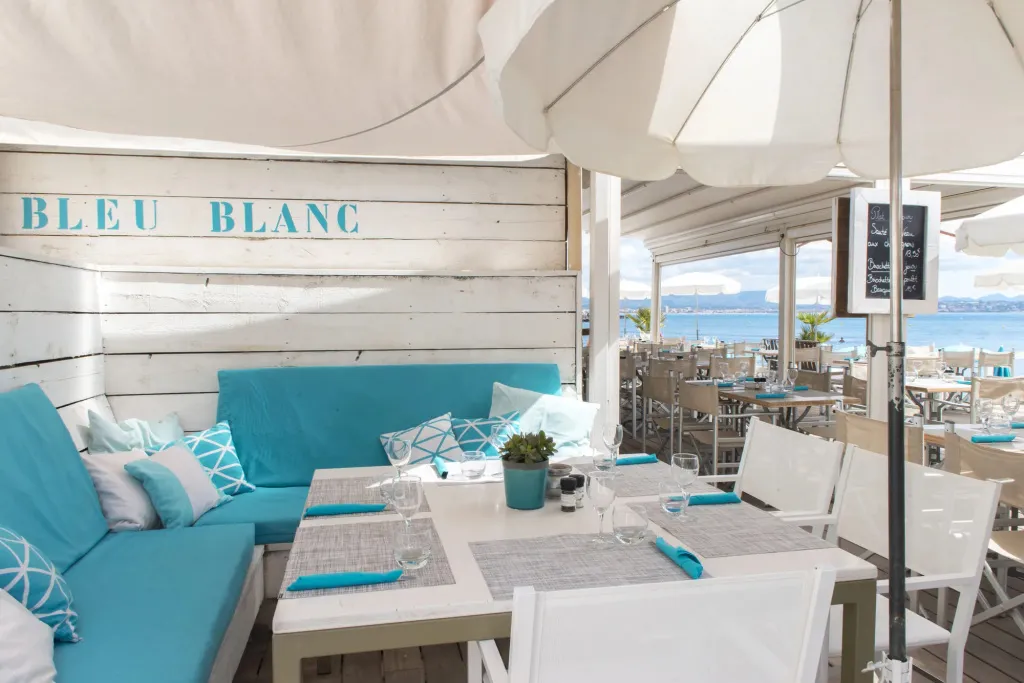 Terrasse de restaurant avec vue sur la mer et mobilier blanc et turquoise.