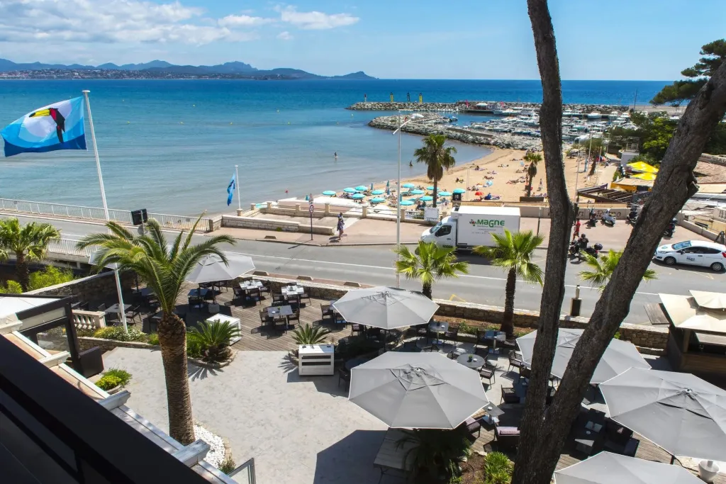 Terrasse ombragée avec tables et parasols donnant sur la mer et une plage.