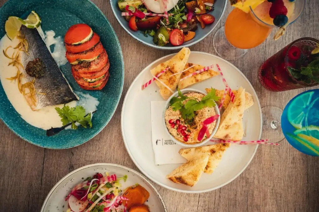 Assortiment de plats colorés et de boissons rafraîchissantes présentés sur une table en bois.