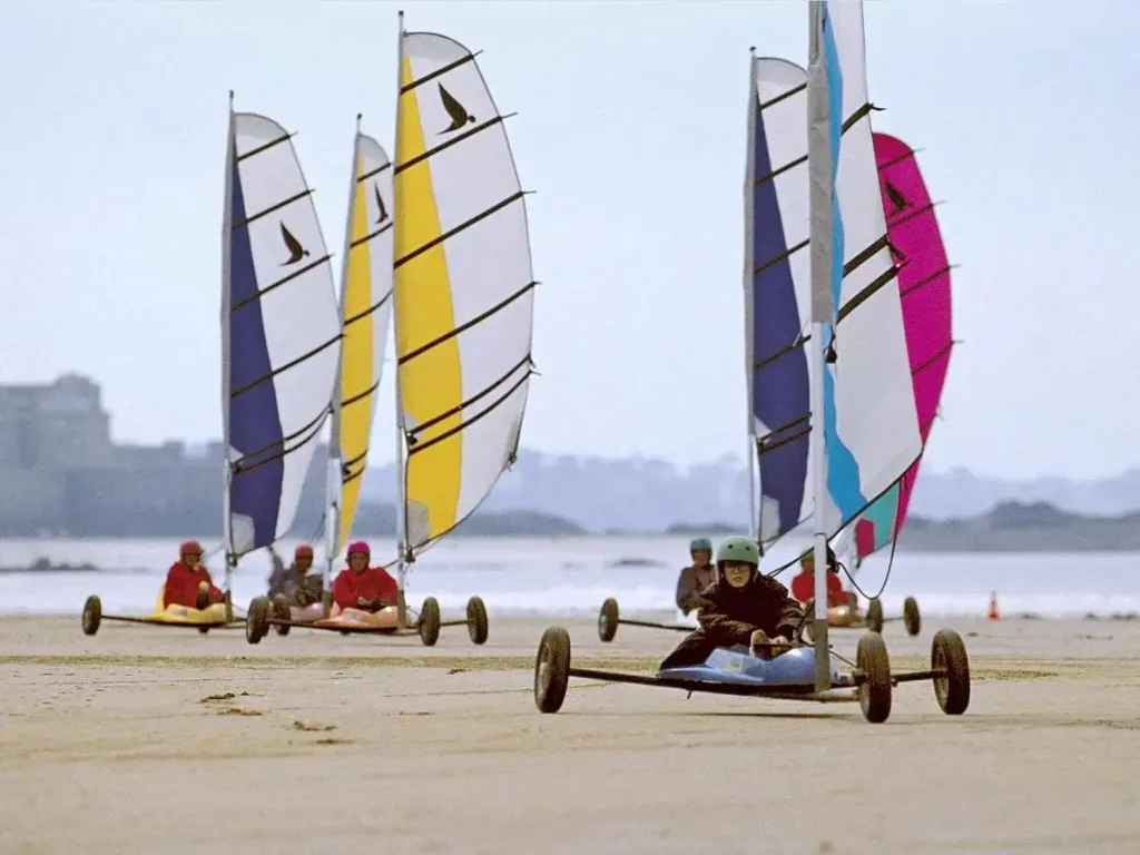 Des personnes pratiquent le char à voile sur une plage de sable.